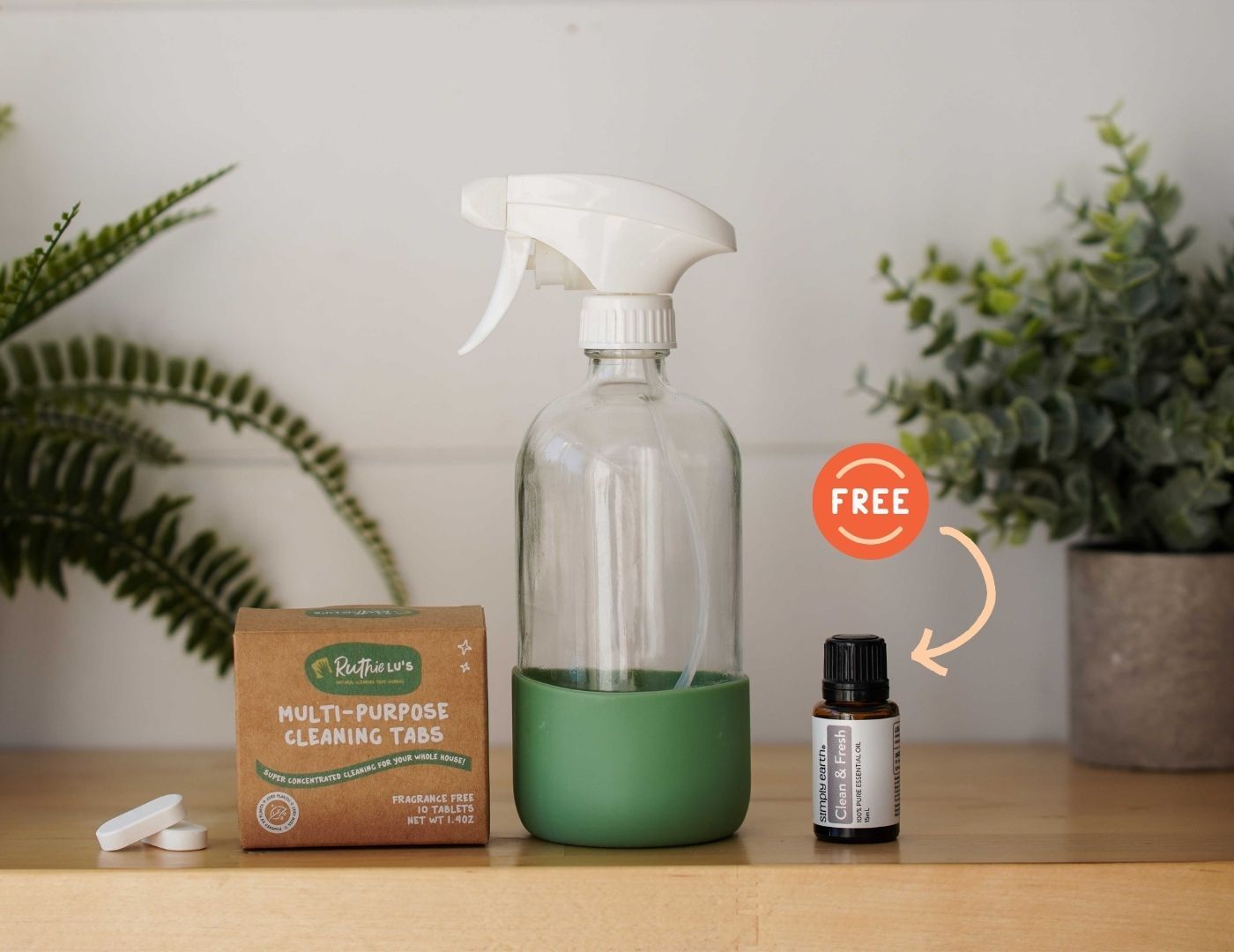 A cleaning spray starter set displayed on a wooden surface, including a 16oz glass reusable spray bottle, two spray heads, 10 cleaning tablets, and a bottle of Simply Earth Clean & Fresh Essential Oil Blend.