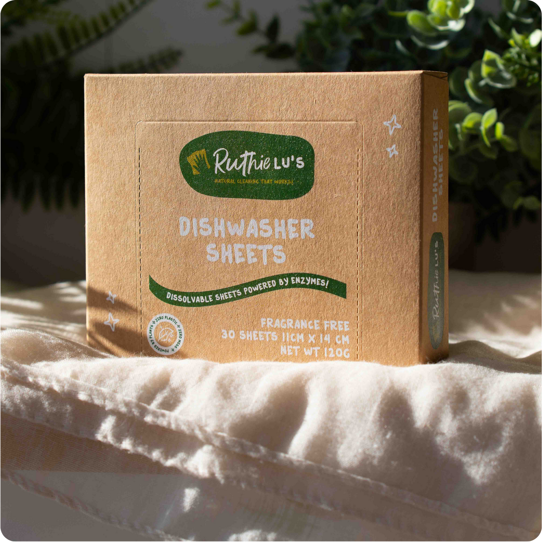 Box of Ruthie Lu's dishwasher sheets on a white surface with greenery in the background. A plastic-free natural cleaning product for streak-free, eco-conscious cleaning.
