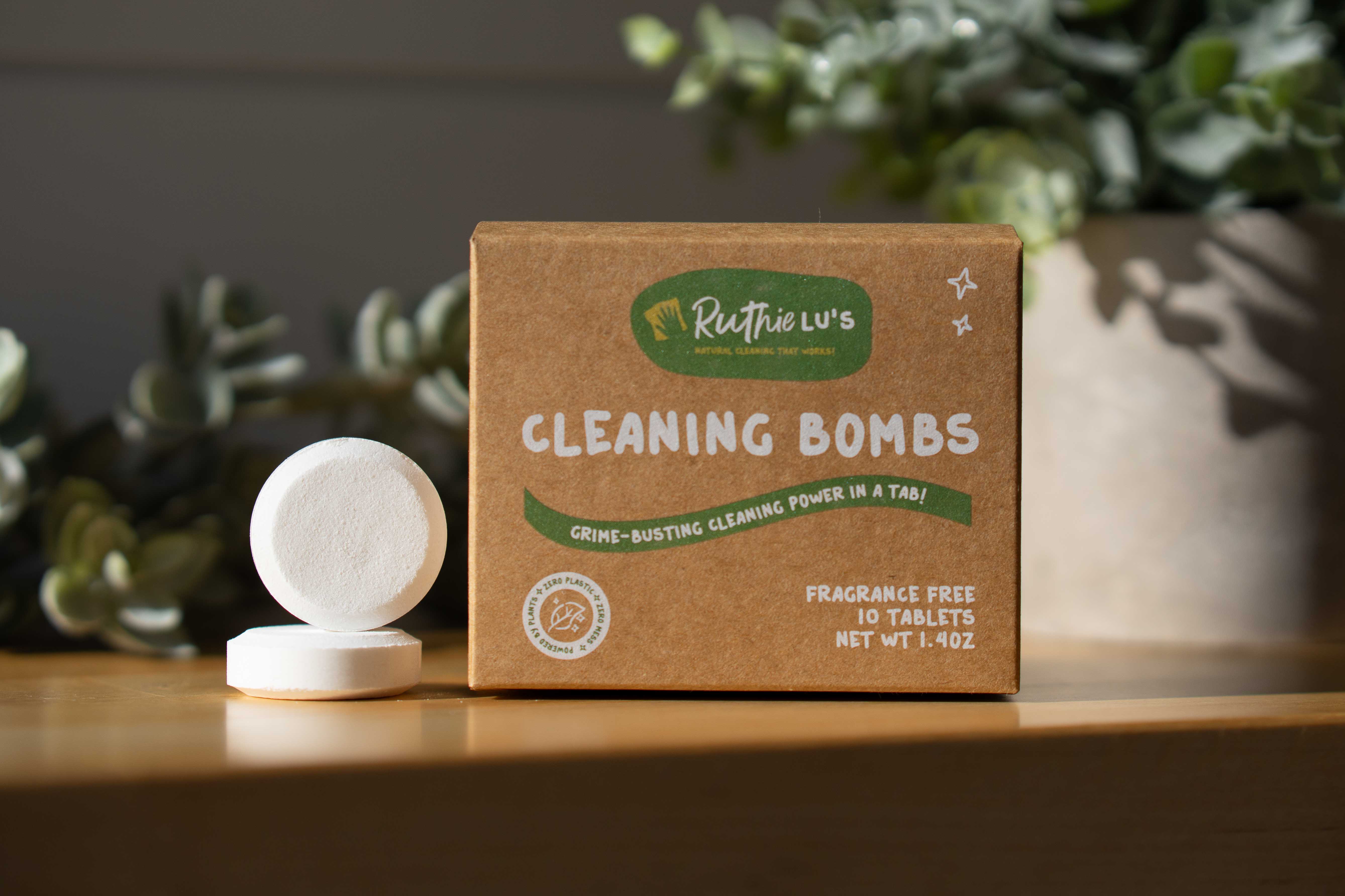 A box of Ruthie Lu’s Cleaning Bombs with individual bombs visible in front of the box. The product is designed for cleaning purposes and the packaging is eco-friendly. Part of a natural cleaning product and bathroom cleaner bomb, safe, eco-friendly, and effective toilet cleaner bomb solution for home cleaning.”