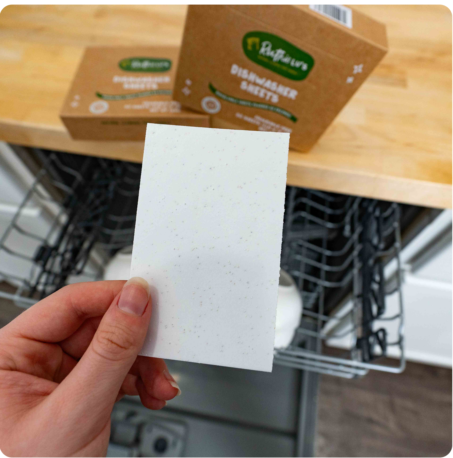 Hand holding a Dishwasher Sheet, a safe, plant-based natural cleaning product for eco-friendly, streak-free dishwashing.