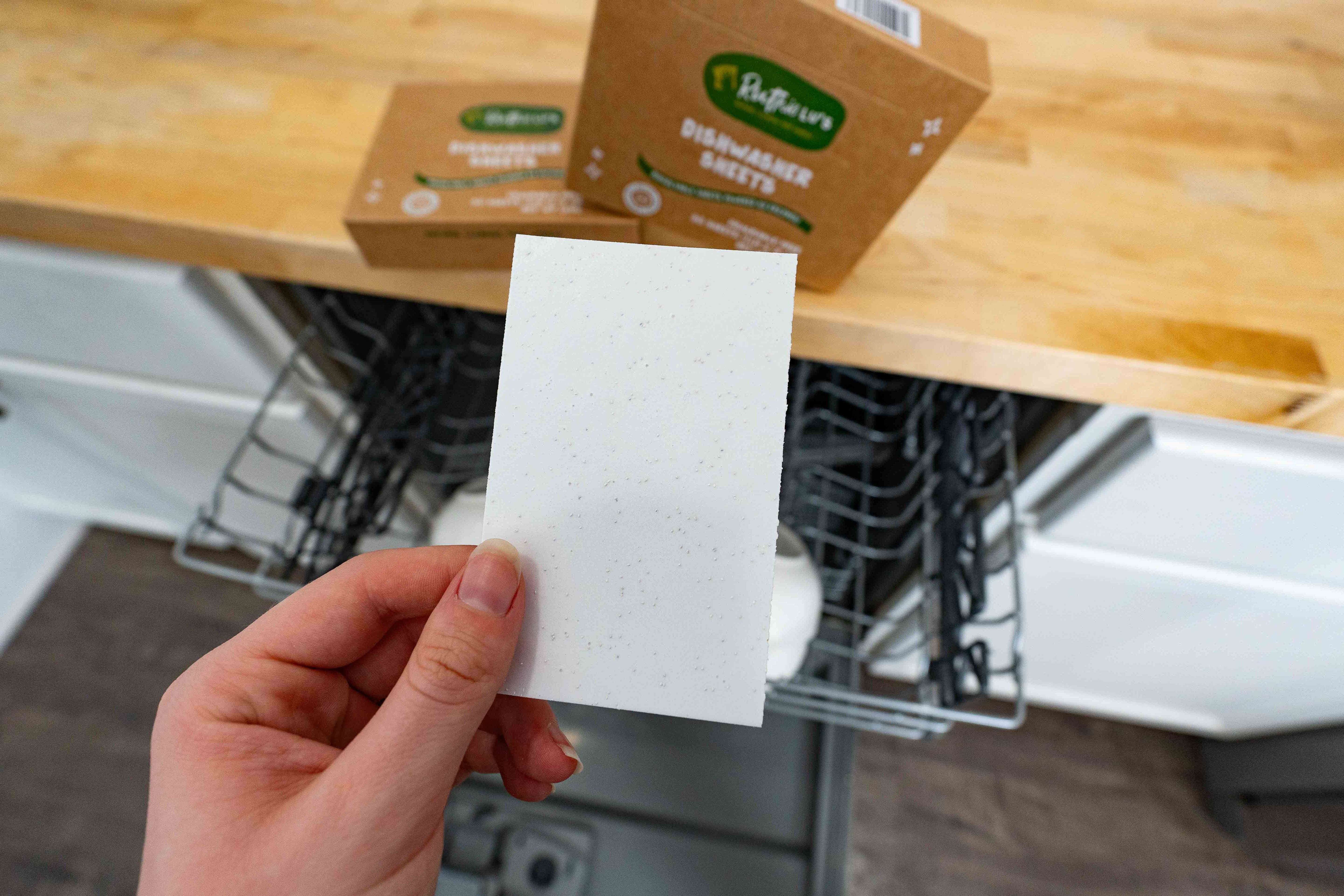 Hand holding a Dishwasher Sheet, a safe, plant-based natural cleaning product for eco-friendly, streak-free dishwashing.